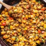 Mexican ground beef and potatoes in a skillet with a wooden spoon.