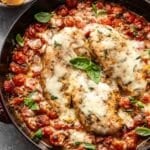 Cherry tomatoes and baked chicken breasts topped with melted mozzarella in a skillet.