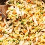 Serving spoon scooping up creamy chicken and noodles out of a skillet.