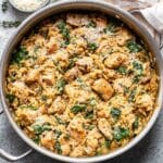 Parmesan orzo and chicken in a skillet with a bowl of parmesan cheese behind it.