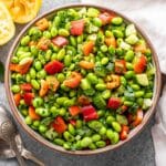 Edamame salad in a white salad bowl with serving spoons next to it and a halved lemon.
