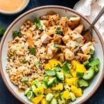 Thai peanut chicken on top of rice with mango cucumber salsa in a white bowl.