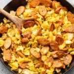 Sauteed cabbage and sausage in a skillet with a wooden spoon.