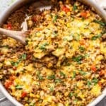 Cheesy ground beef and rice in a skillet with a wooden serving spoon.