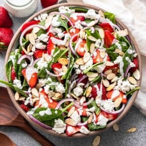 Strawberry spinach salad with goat cheese, red onions, and almonds in a salad bowl topped with creamy poppy seed dressing.