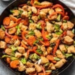 Chicken stir fry in a skillet with peppers, carrots, and broccoli.