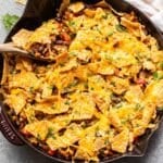 Turkey taco mixture in a skillet with a wooden serving spoon topped with tortilla chips and melted cheese.