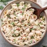 Tuna pasta salad in a white serving bowl with a wooden spoon in it.