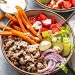 Burger bowl topped with sweet potato fries, tomatoes, pickles, red onions, and burger sauce.