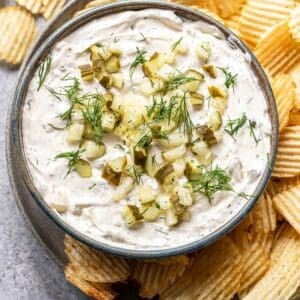 dill pickle dip in a bowl on a plate with potato chips.