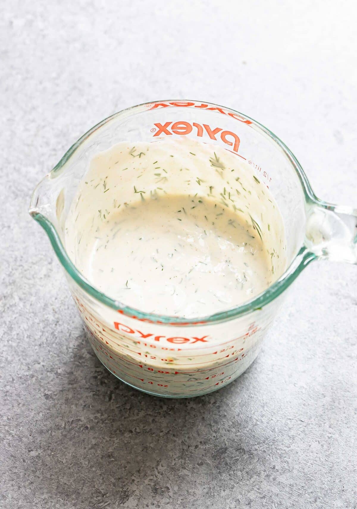 Creamy dill dressing in a glass measuring cup.