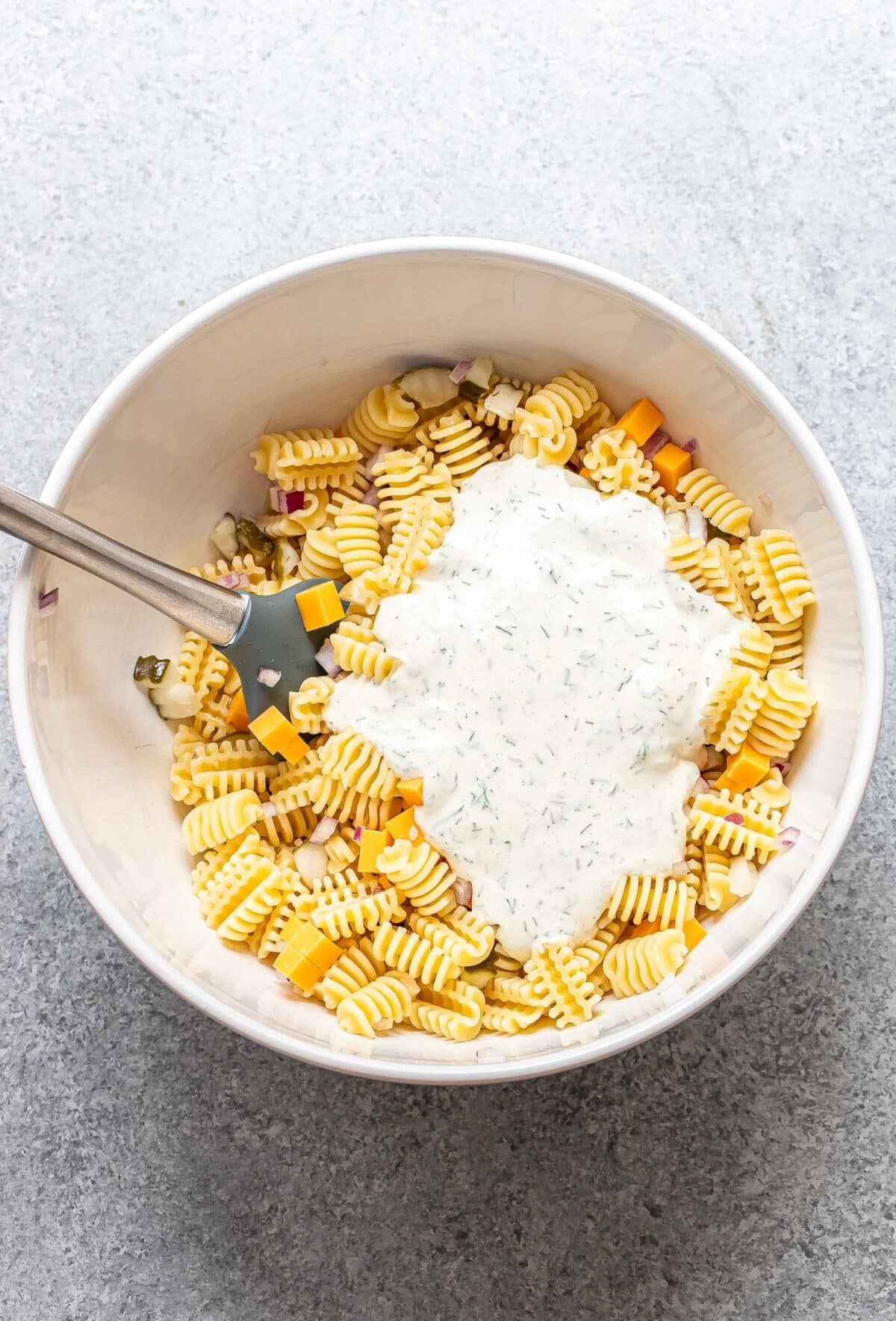 Pickle pasta salad with creamy dill dressing on top before it's been mixed in.