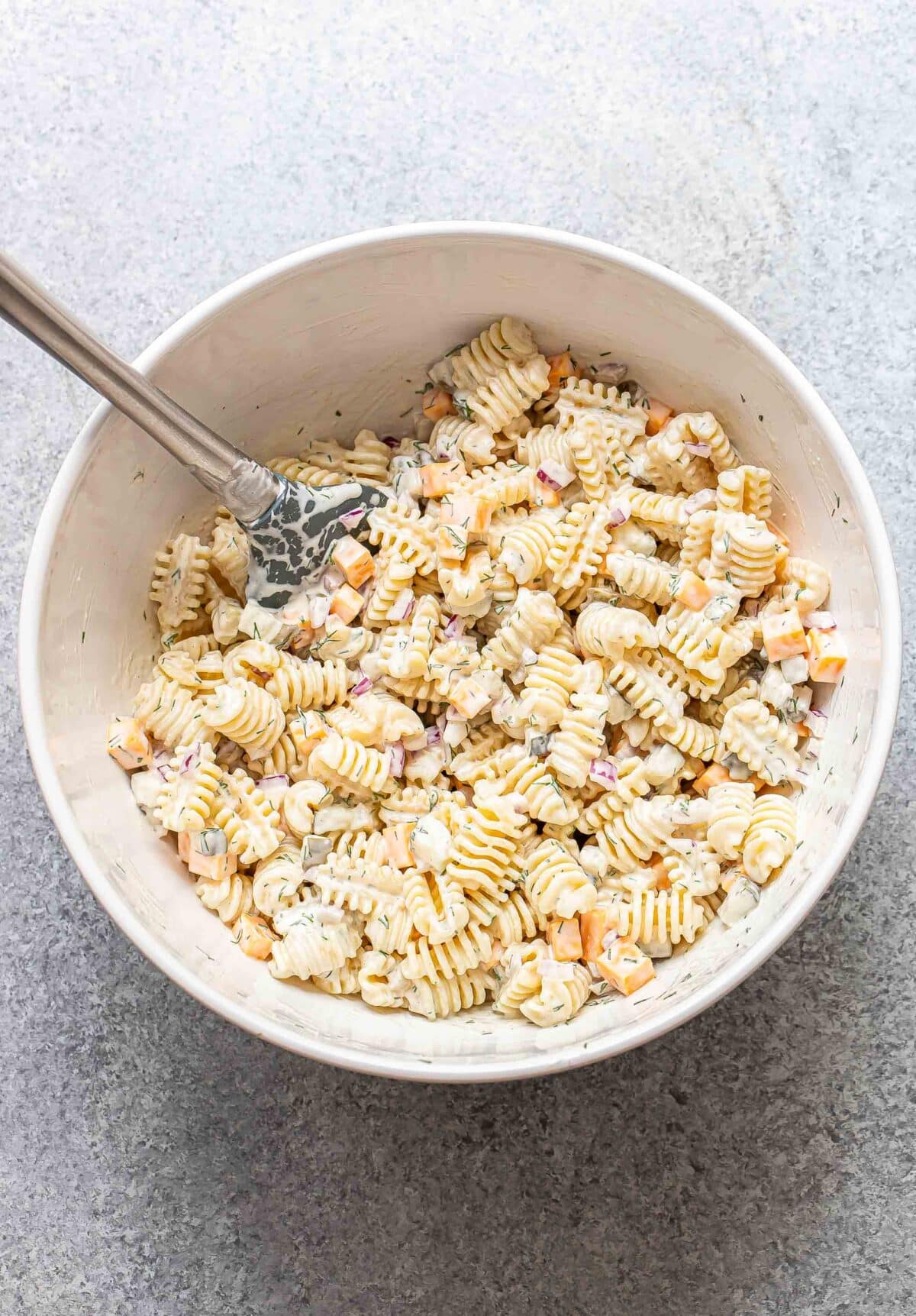 Dill pickle pasta salad in a white mixing bowl with a rubber spatula in the bowl.