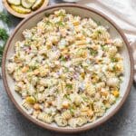 Creamy dill pickle pasta salad in a white salad bowl with a bowl of pickles behind it.