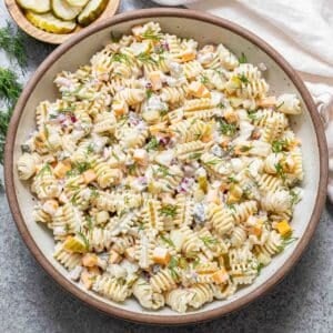 Creamy dill pickle pasta salad in a white salad bowl with a bowl of pickles behind it.
