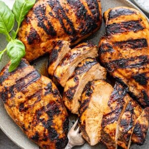 Four grilled chicken breasts on a gray plate with a fork.