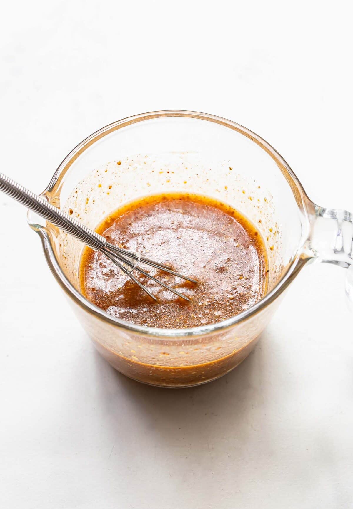 Honey mustard chicken marinade in a glass measuring cup with a whisk.