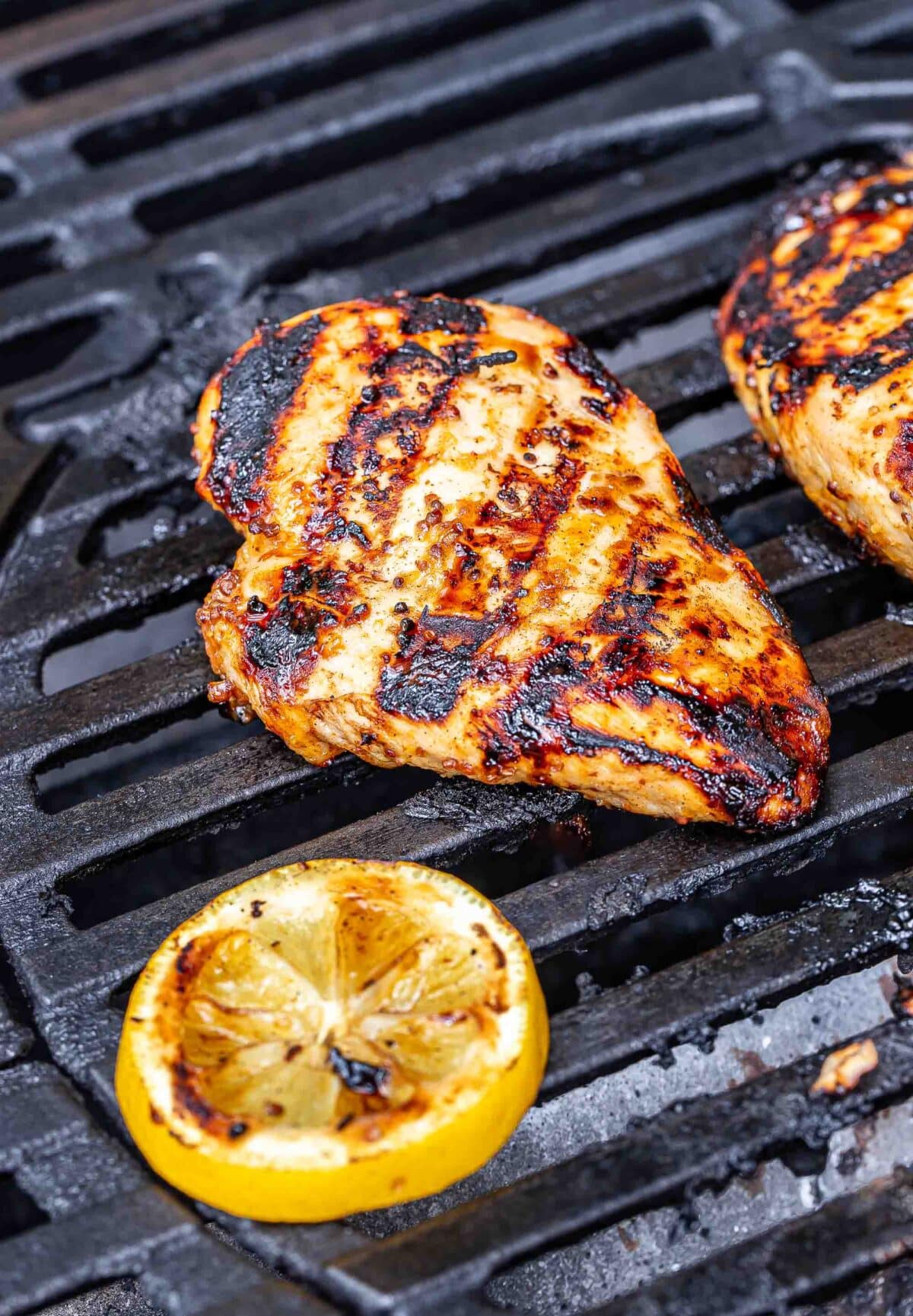 Grilled chicken breast on the grill with a lemon slice.