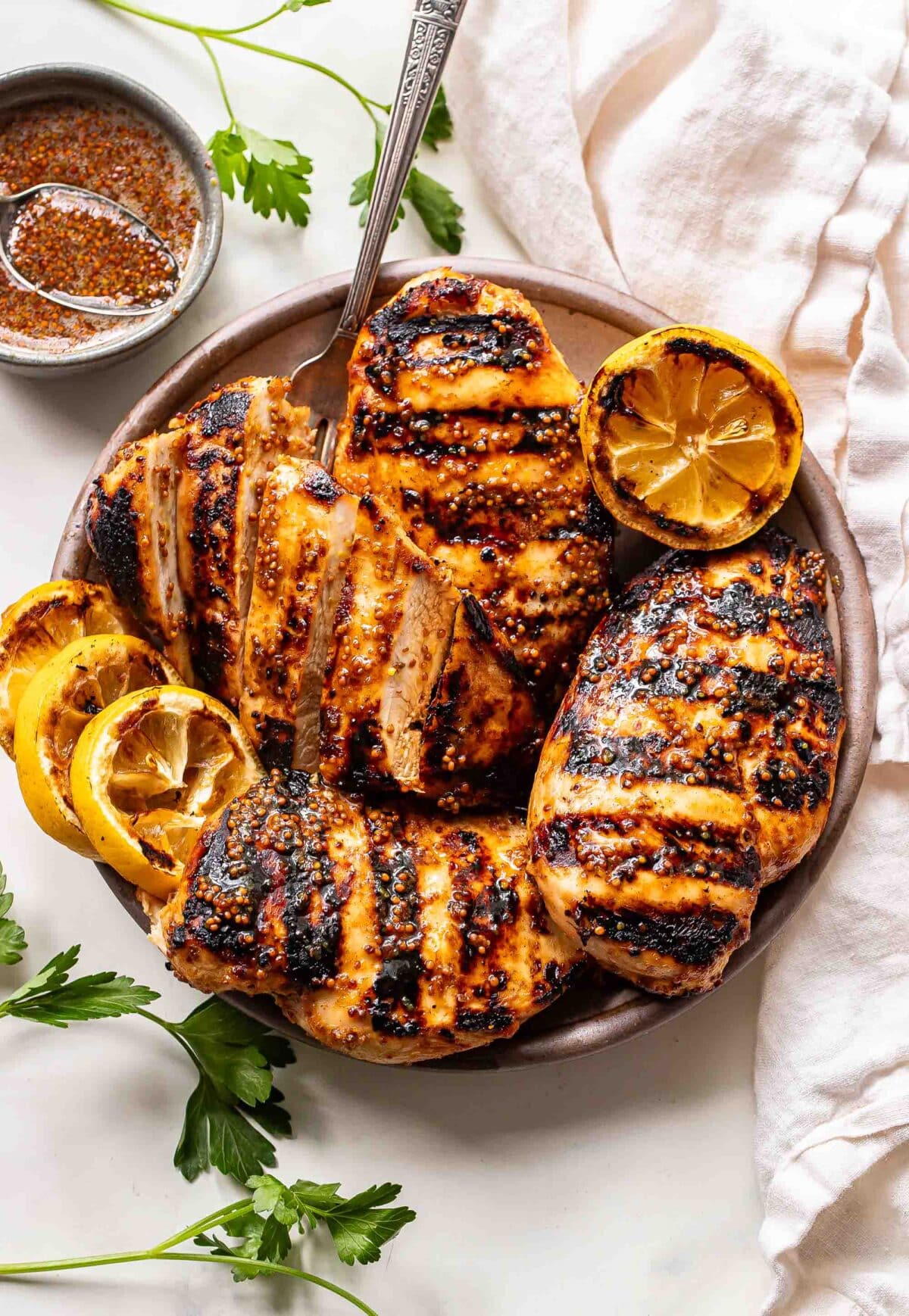 Four honey mustard grilled chicken breasts on a plate with grilled lemons.