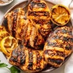 Four honey mustard grilled chicken breasts on a plate with grilled lemons.