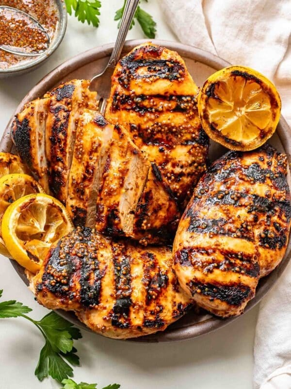 Four honey mustard grilled chicken breasts on a plate with grilled lemons.
