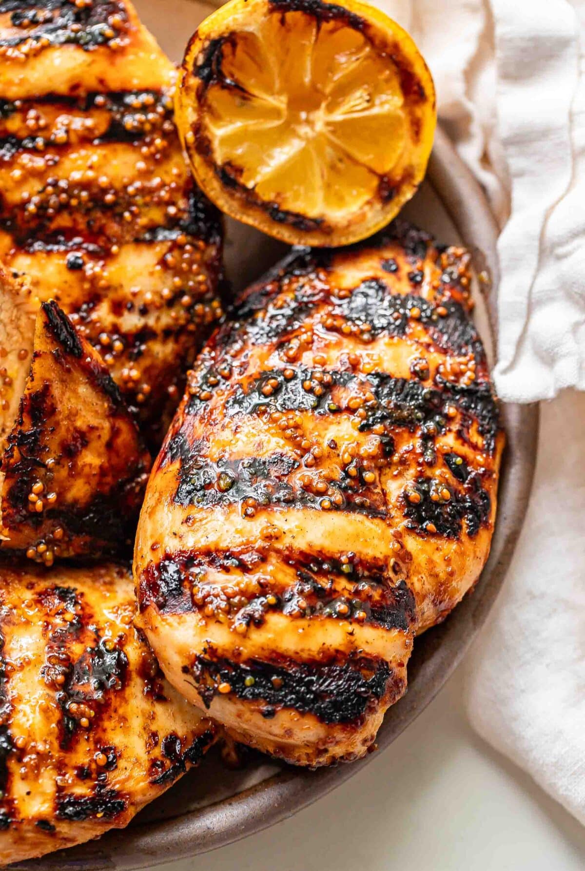 Honey mustard grilled chicken on a plate with grilled lemon.