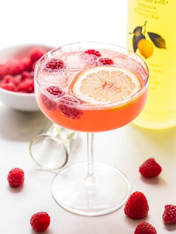 Raspberry limoncello spritz in a coupe glass with fresh raspberries and a lemon slice in it for garnish.