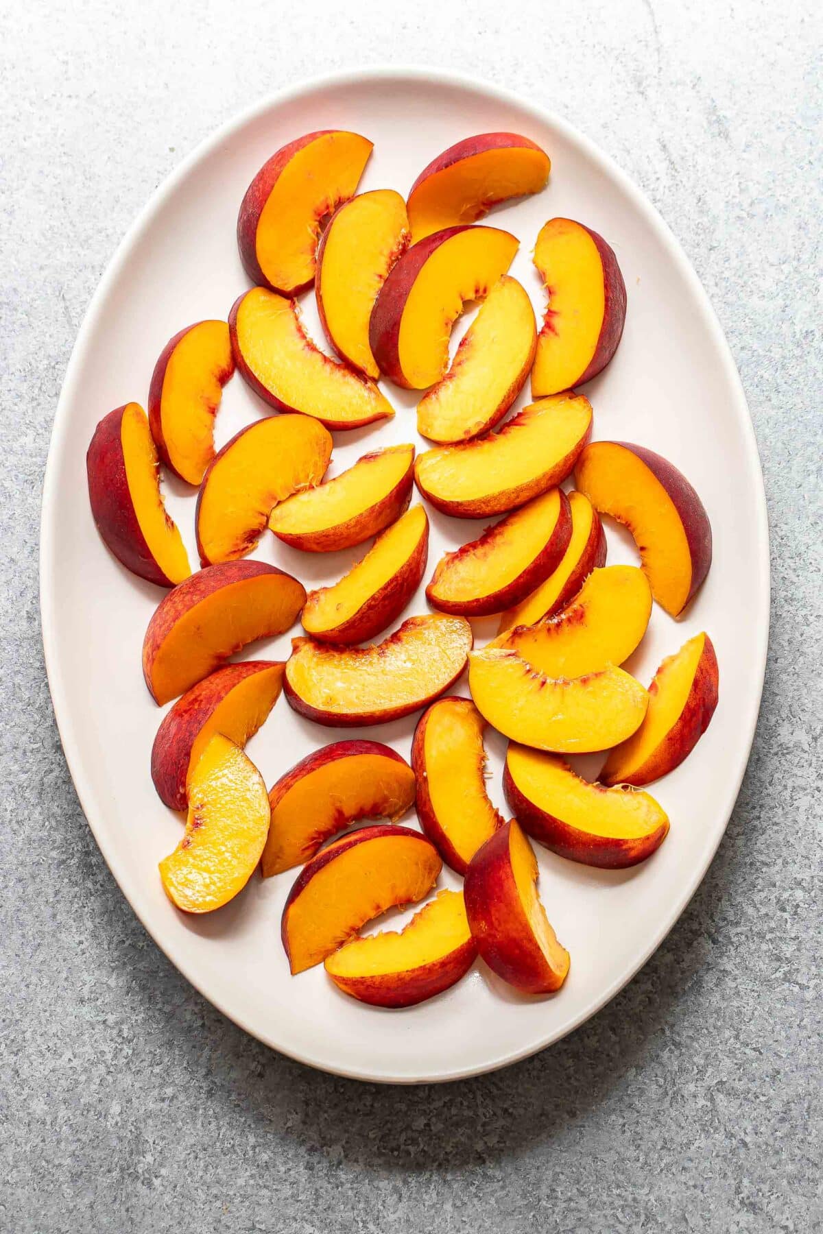 Sliced peaches on a white oval serving plate.