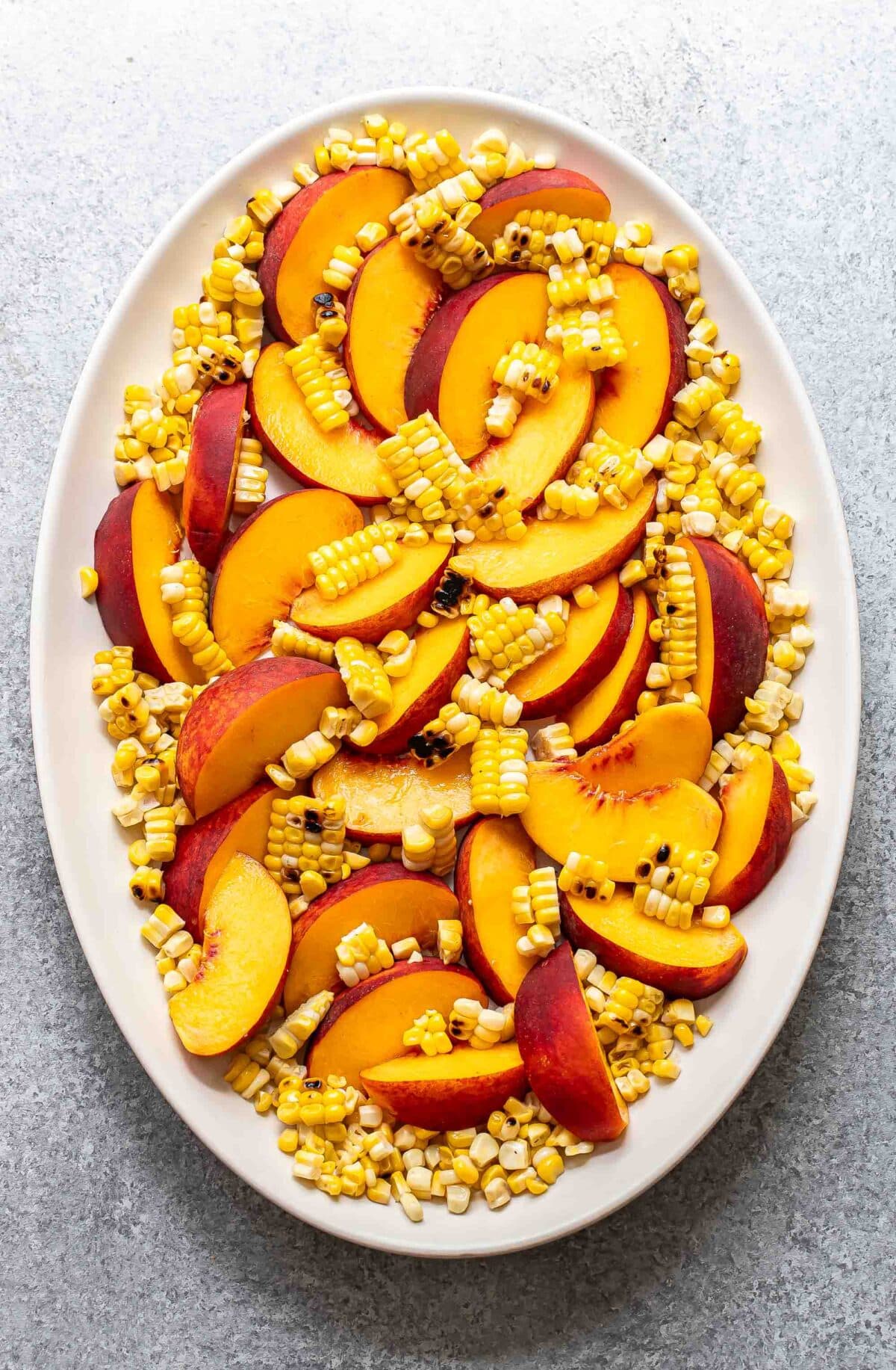 Sliced peaches and corn kernels on a white oval serving plate.