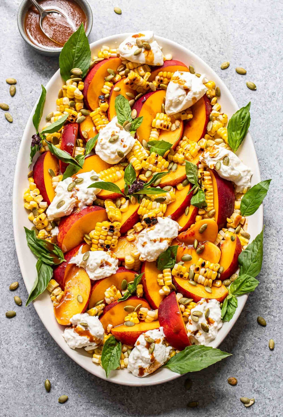 Burrata peach salad with corn and basil on an oval serving plate.