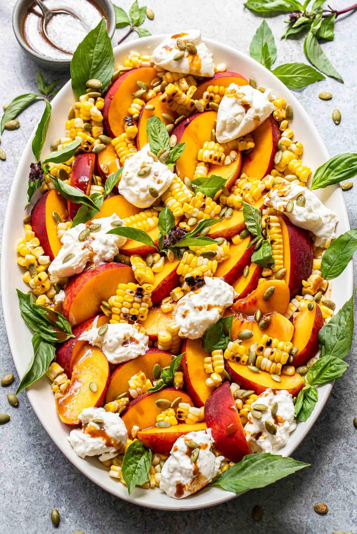 Burrata peach salad with corn and basil on an oval serving plate.