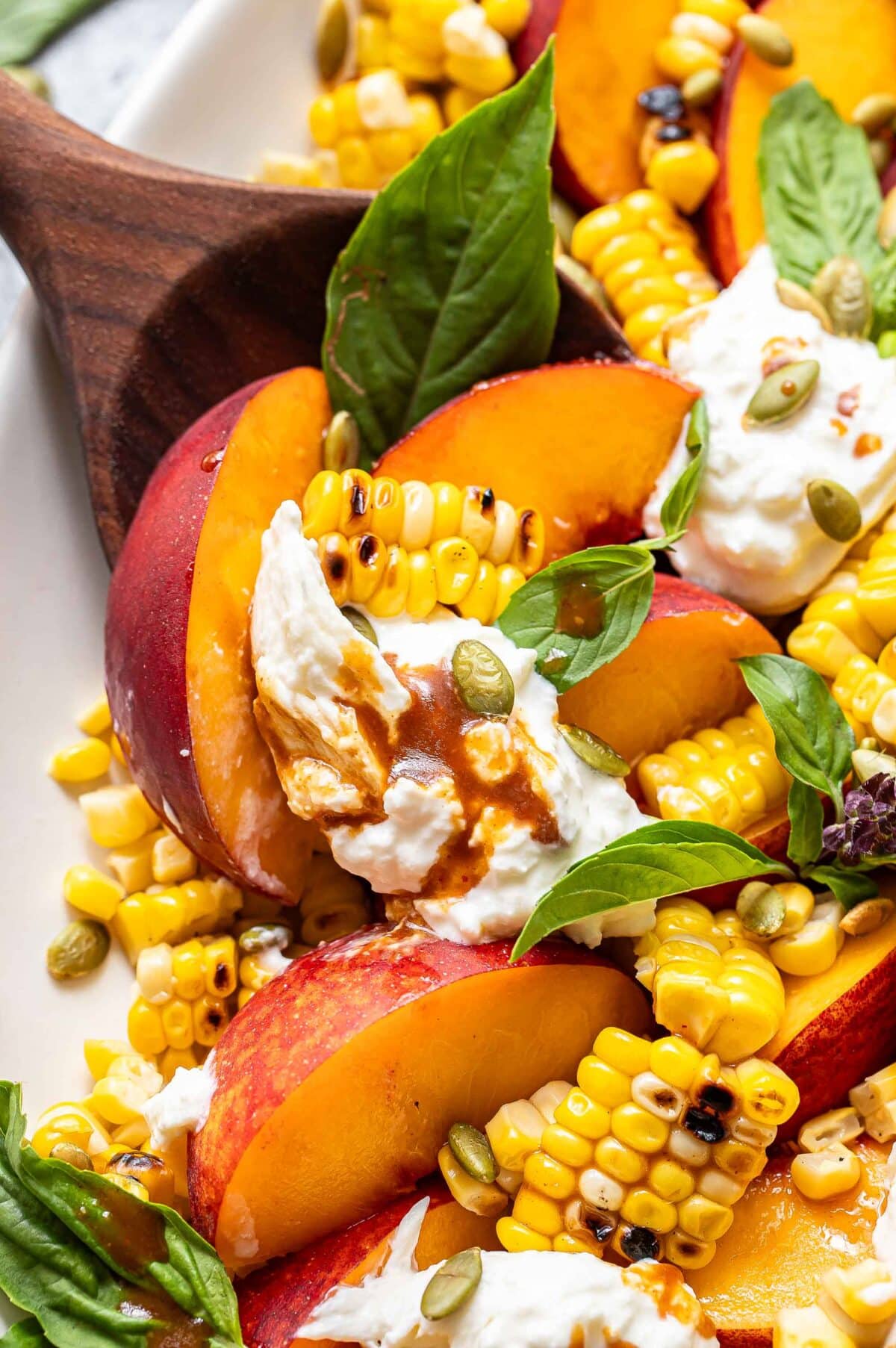 Burrata peach salad on a wooden serving spoon.