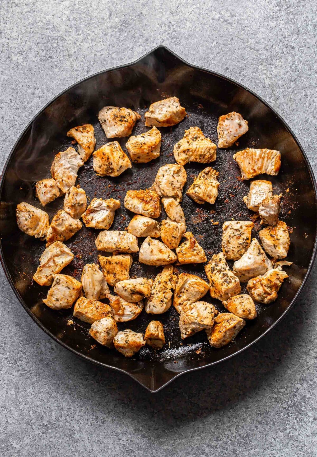 Chunks of cooked chicken in a skillet.