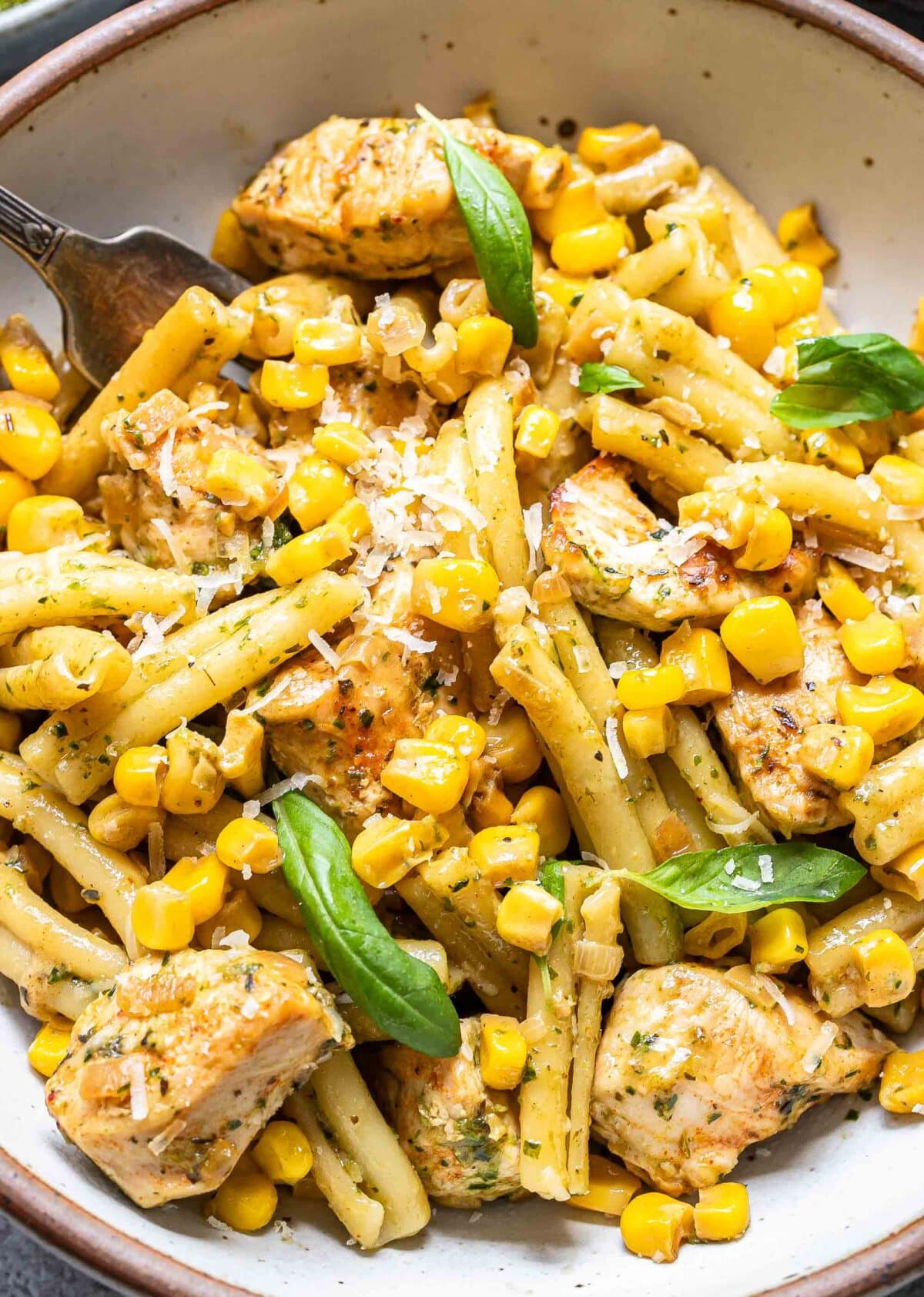Chicken corn pasta in a bowl topped with parmesan cheese and basil leaves.