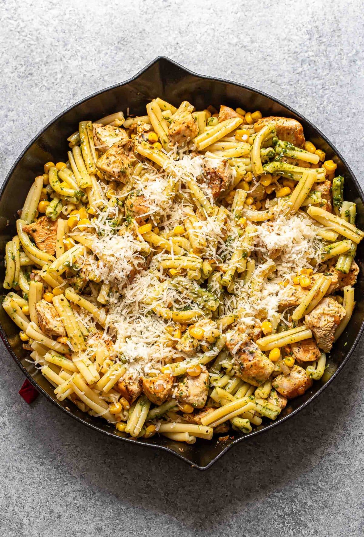 Creamy pesto chicken, corn, and pasta topped with parmesan cheese.