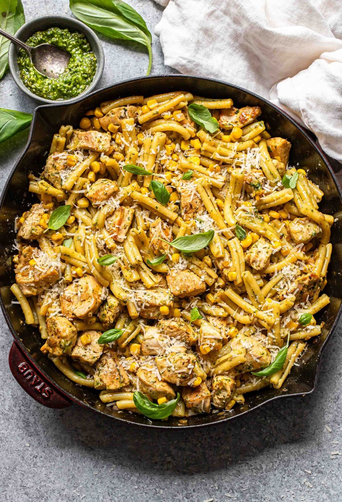 Chicken and corn pasta topped with parmesan cheese and basil leaves in a skillet.