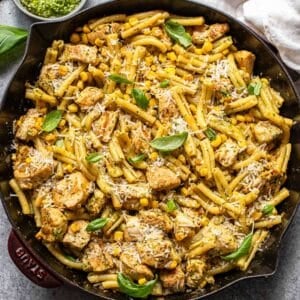 Chicken and corn pasta topped with parmesan cheese and basil leaves in a skillet.