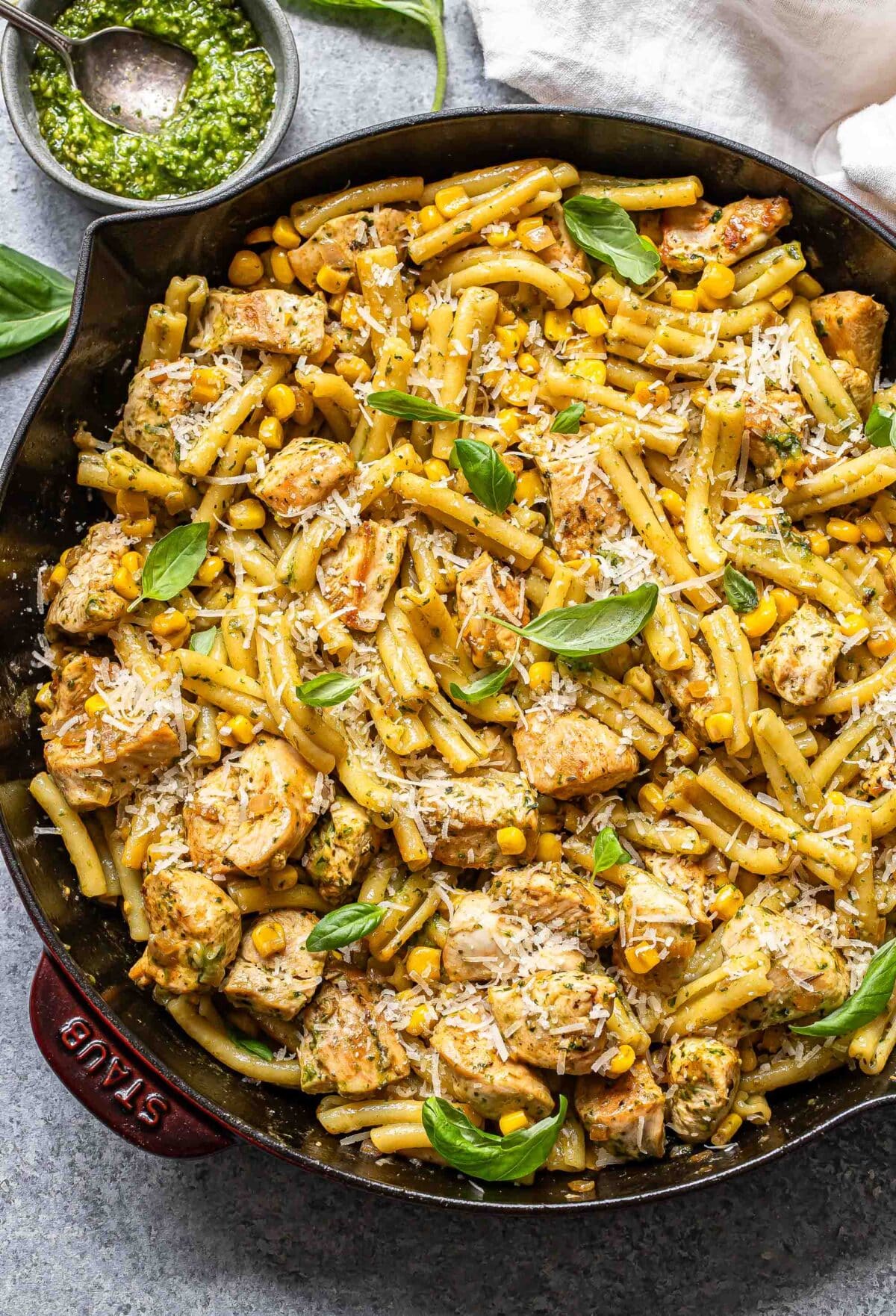 Chicken and corn pasta topped with parmesan cheese and basil leaves in a skillet.