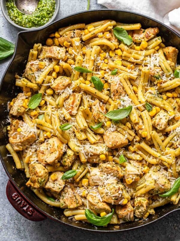 Chicken and corn pasta topped with parmesan cheese and basil leaves in a skillet.