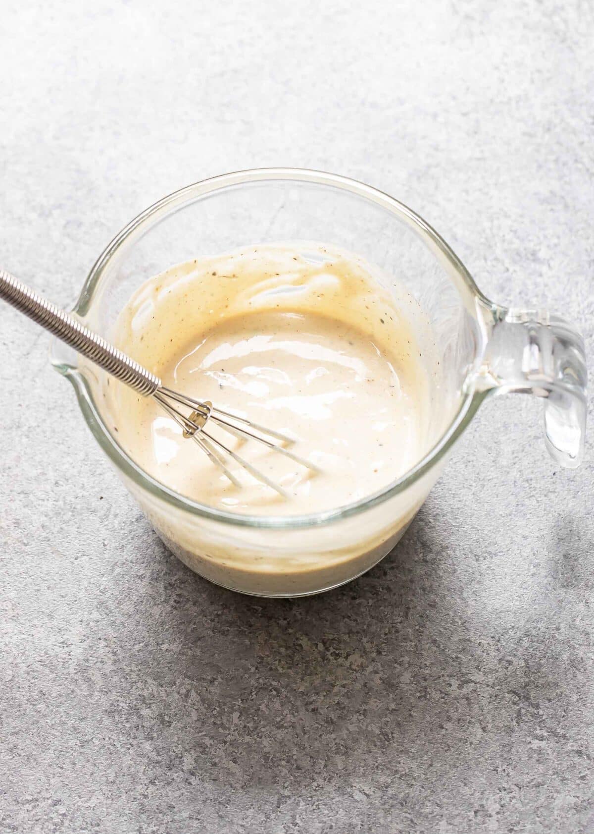 Dill pickle dressing in a glass measuring cup with a whisk.
