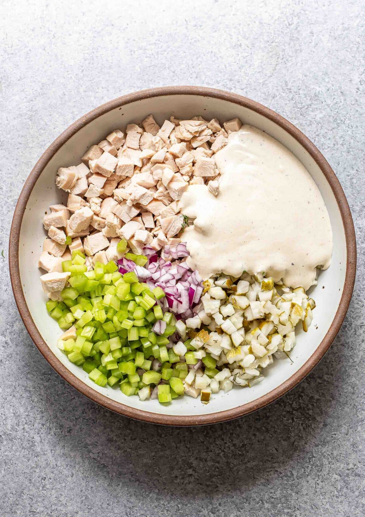 Chicken, celery, red onion, pickles, dill, and a creamy pickle dressing in a white bowl.