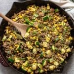 Pesto ground beef with zucchini and corn in a skillet with a wooden serving spoon.