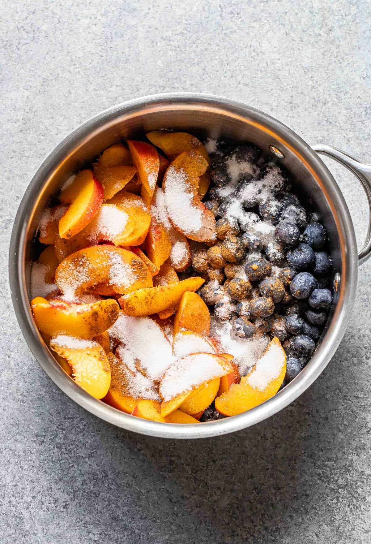 Sliced peaches, blueberries, and sugar in a saucepan.