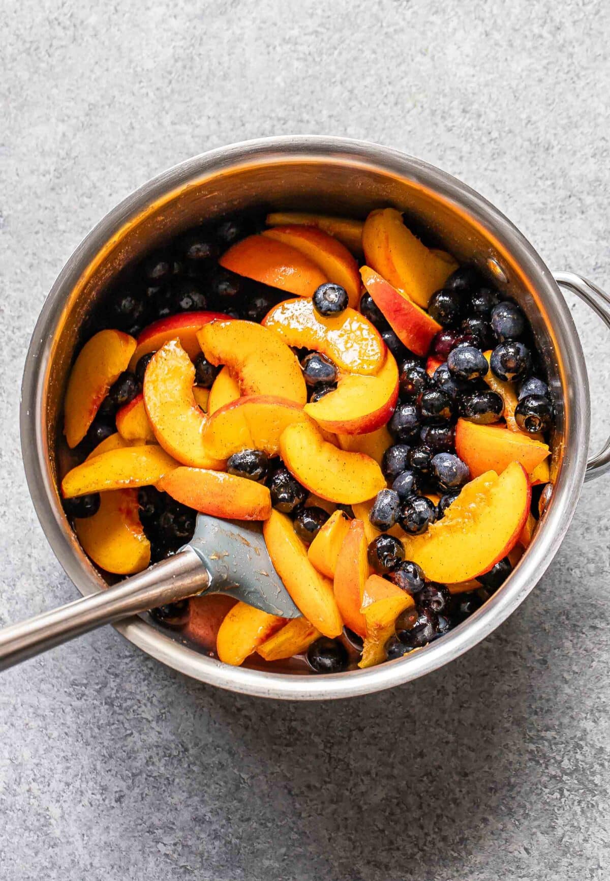 Cooked peaches and blueberries in a saucepan with a spatula.