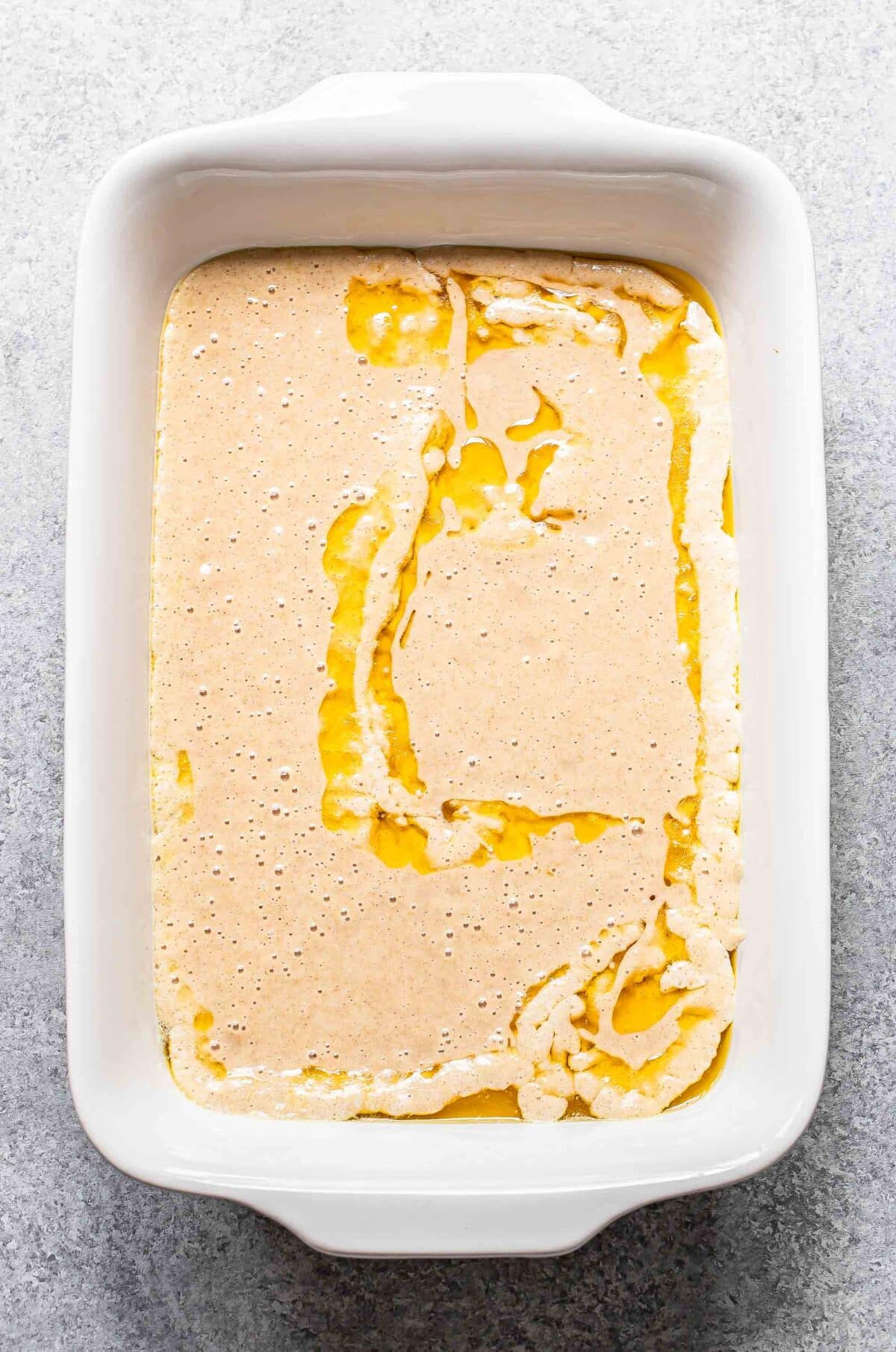 Cobbler batter on top of melted butter in a rectangular baking dish.