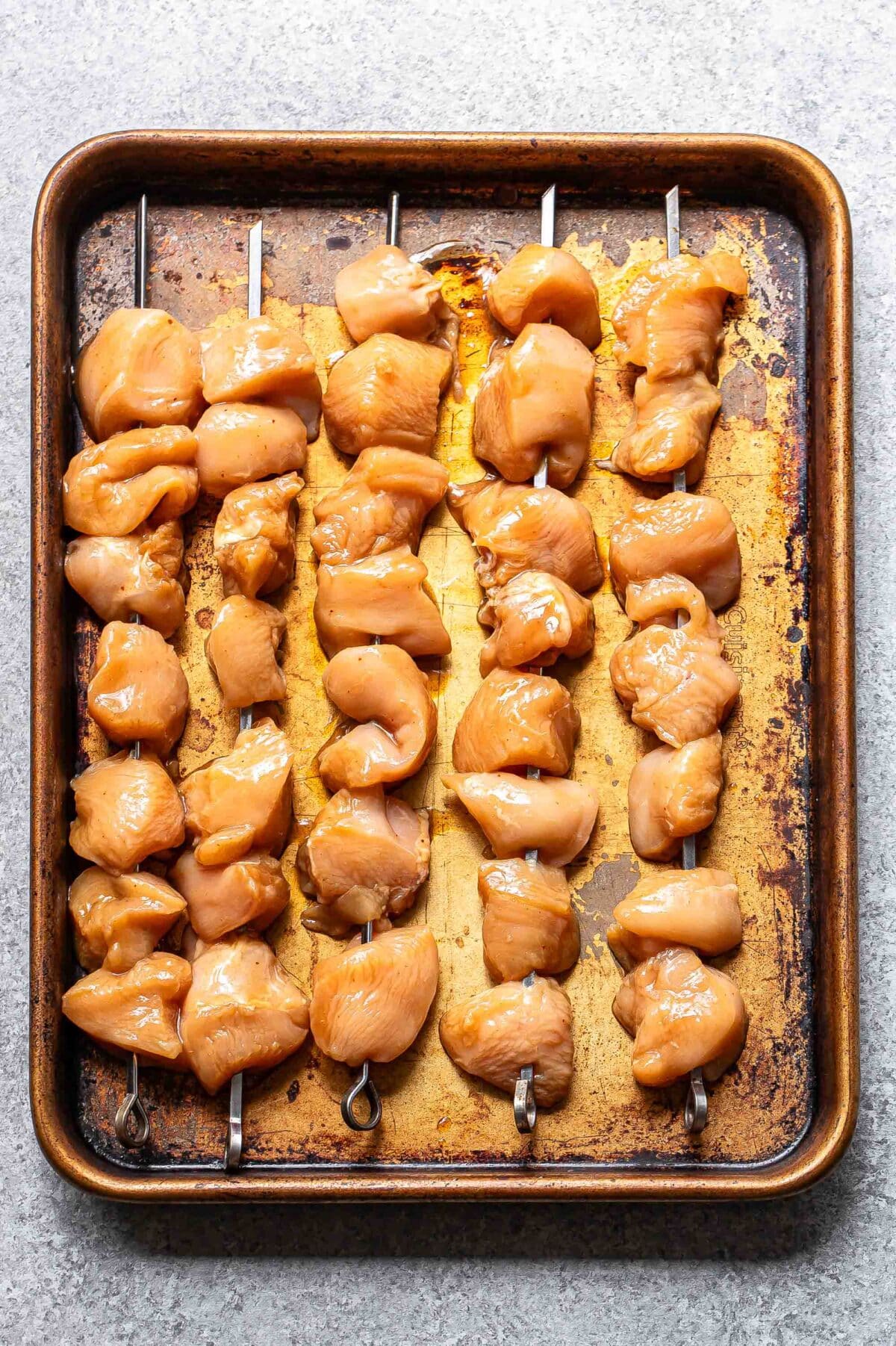 Uncooked teriyaki chicken skewers on a sheet pan.