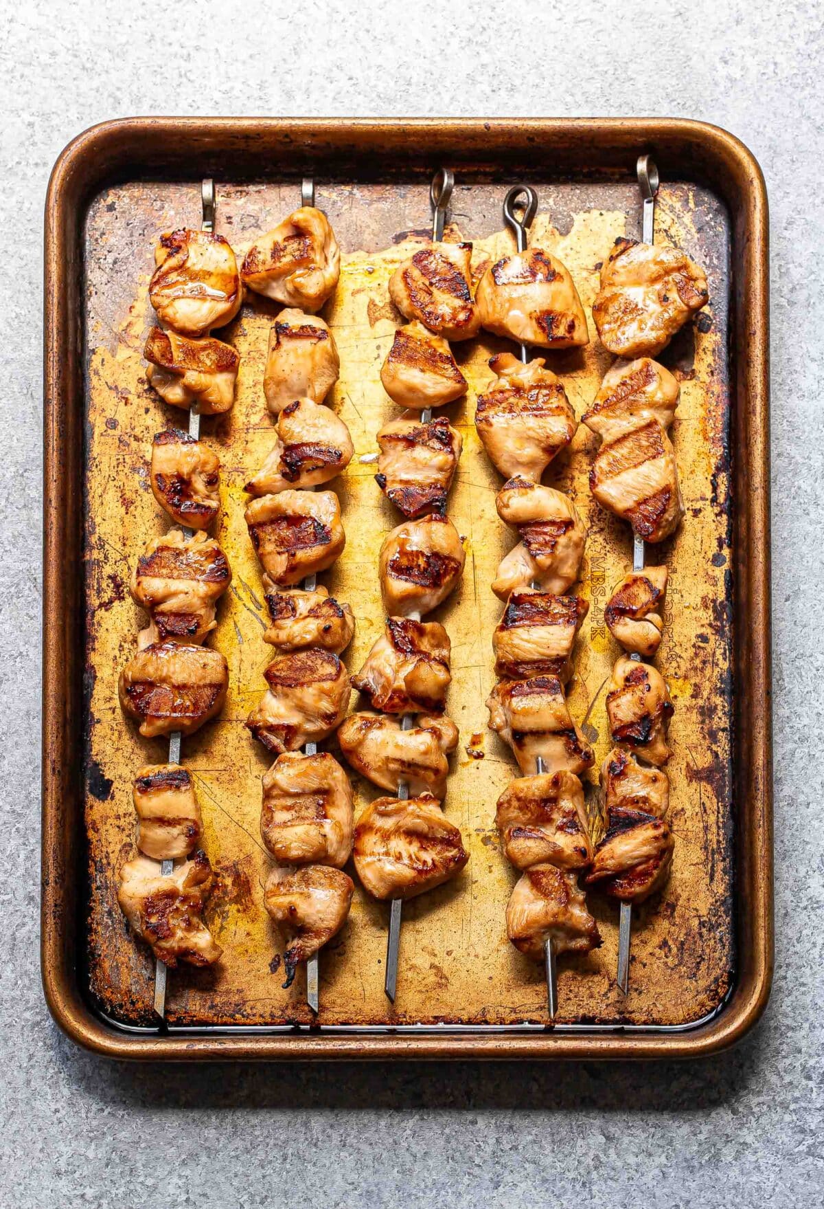 Grilled teriyaki chicken skewers on a sheet pan.