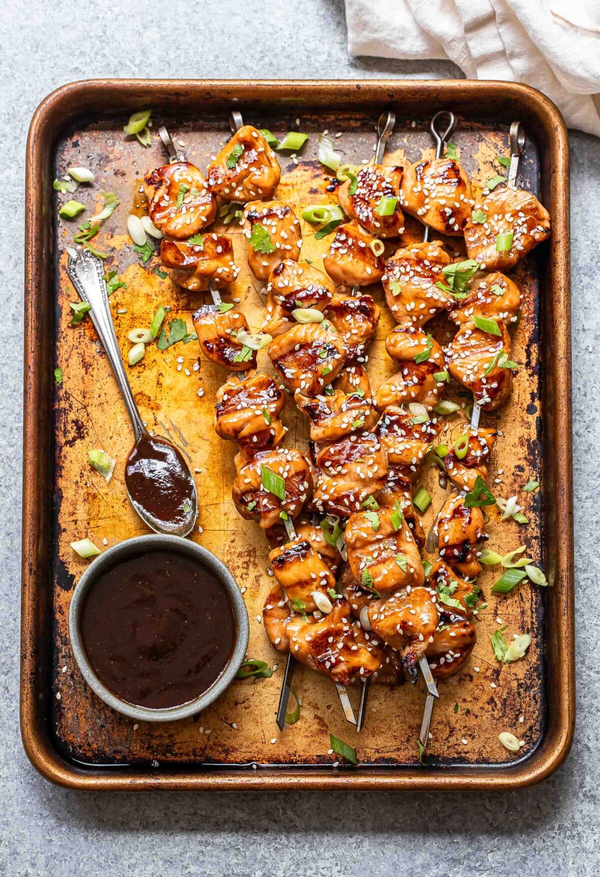 Grilled teriyaki chicken skewers on a sheet pan with a bowl of teriyaki sauce.