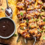 Grilled teriyaki chicken skewers on a sheet pan with a bowl of teriyaki sauce.