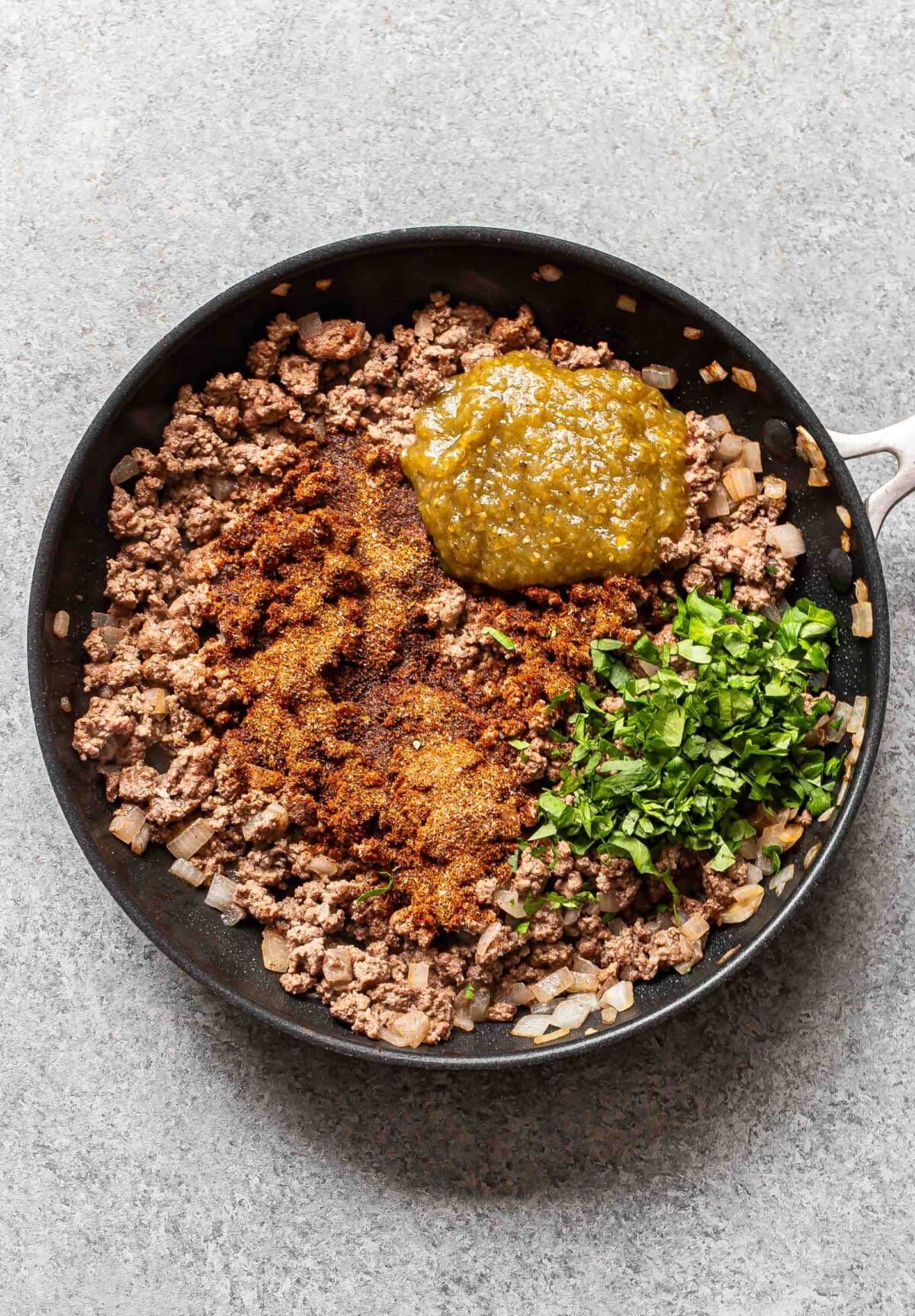 Ground beef topped with spices, salsa, and cilantro in a skillet.
